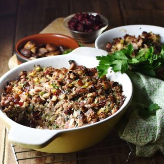 Side view of stuffing in white casserole dish, with green cloth, stuffing in white bowl and chestnuts in brown dish in background.