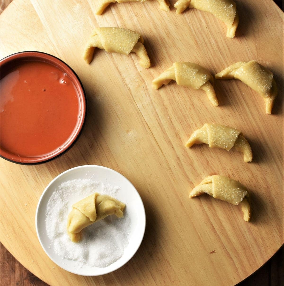 Unbaked rogaliki, saucer with sugar and egg whites in brown dish.