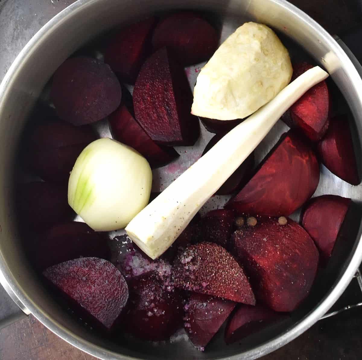 Top down view of peeled beets, celery root, parsley root and onion in large pot.