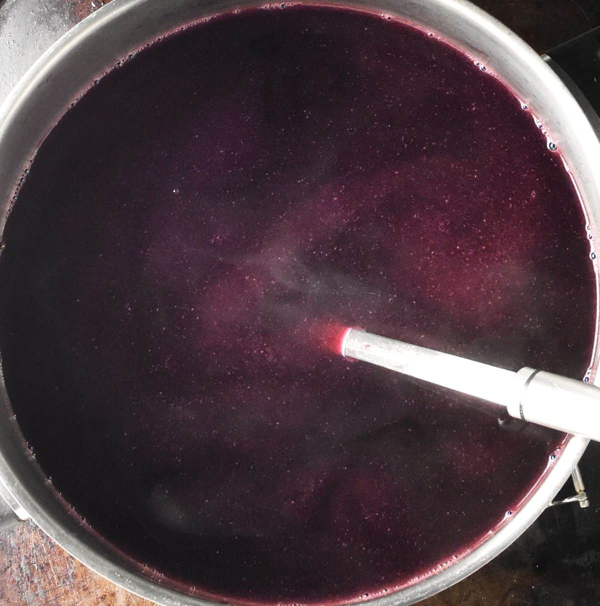 Clear barszcz soup in large metal pot with ladle.