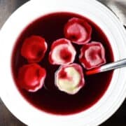 Top down view of Polish barszcz soup with uszka dumplings in white bowl with spoon.