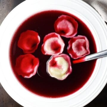 Top down view of Polish barszcz soup with uszka dumplings in white bowl with spoon.