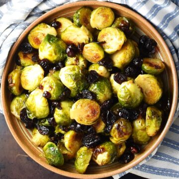 Top down view of roasted brussels sprouts with cranberries in brown bowl.