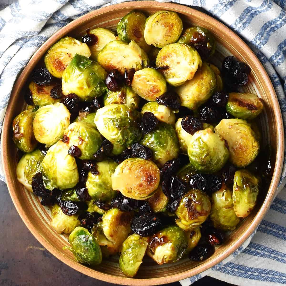 Top down view of roasted brussels sprouts with cranberries in brown bowl.
