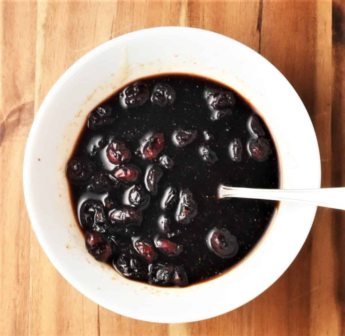 Cranberries in balsamic mixture in white bowl with spoon.
