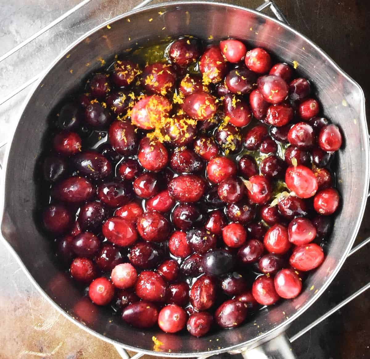 Cranberries, honey and orange zest in metal saucepan.
