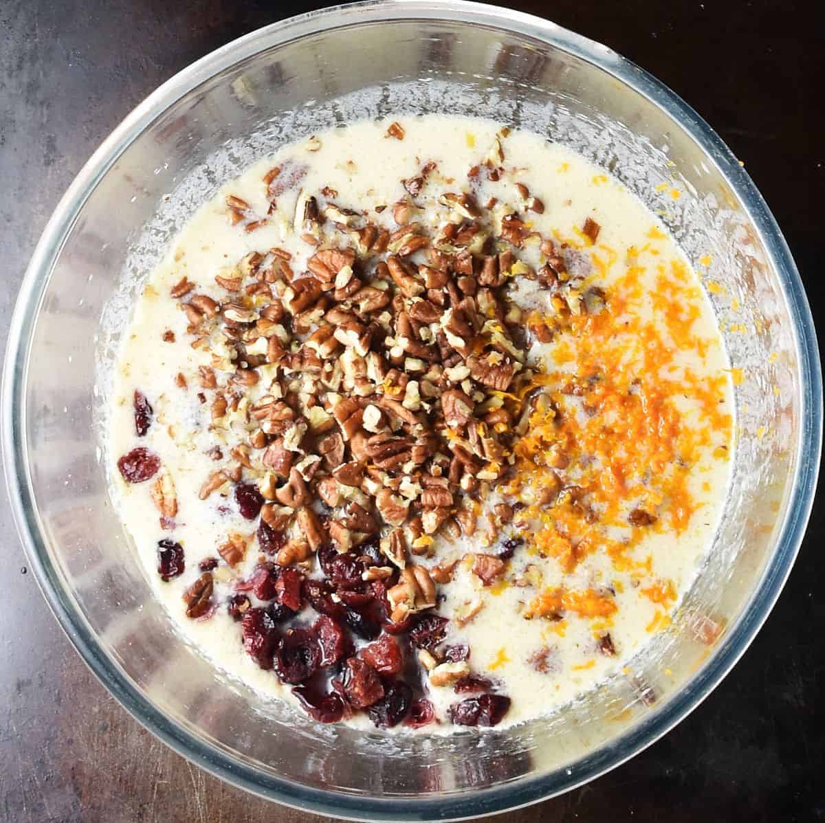 Top down view of muffin batter with dried cranberries, chopped pecans and orange zest.