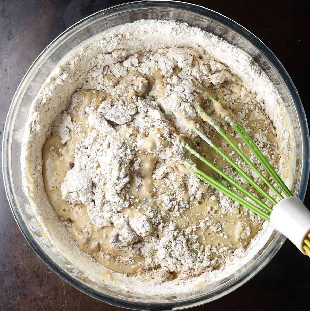 Top down view of dried cranberry muffin batter in glass bowl with whisk.