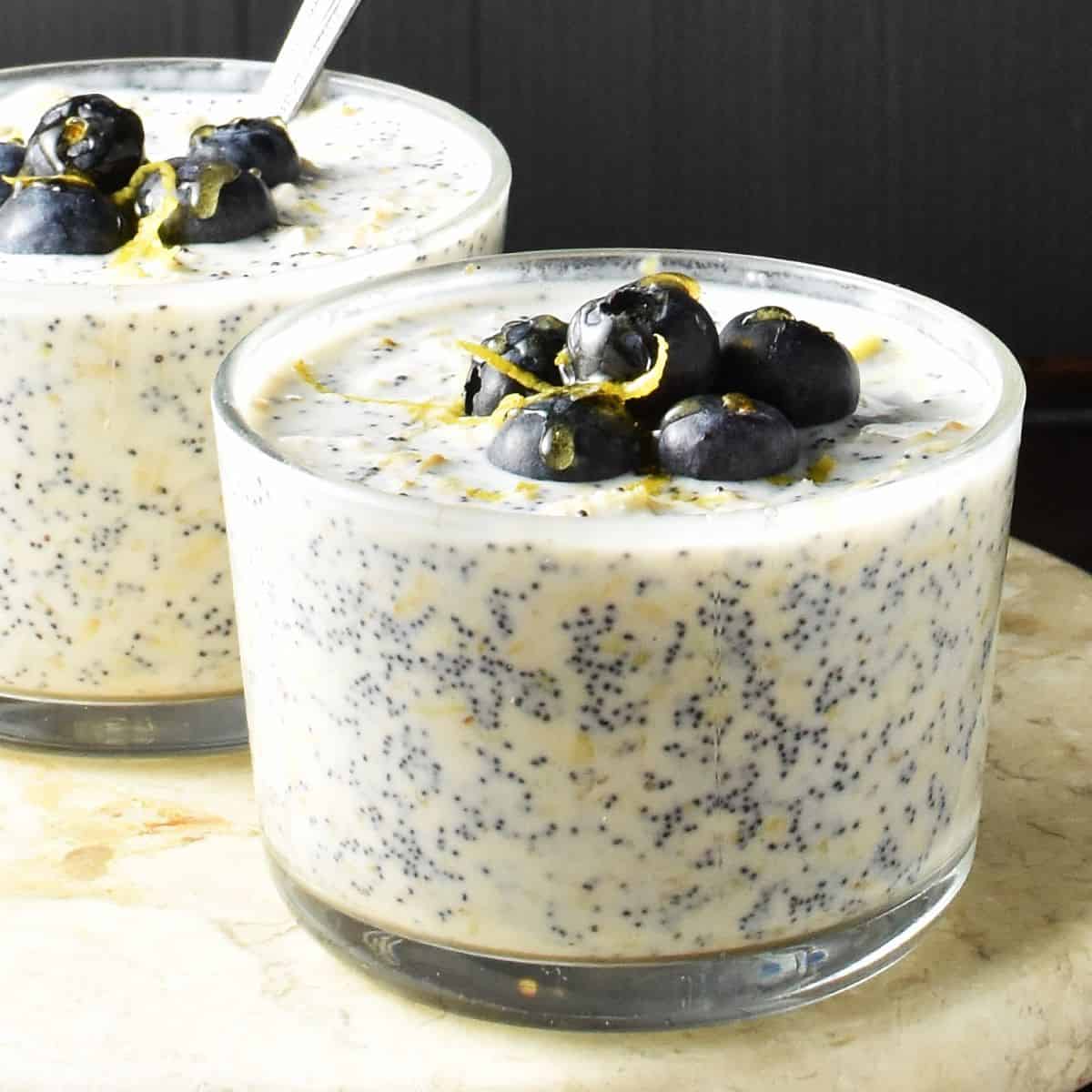 Side view of lemon poppy seed overnight oats in 2 glasses with spoon.