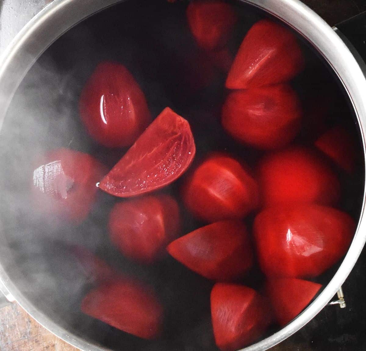 Top down view of cooked beets and vegetables in Polish borscht in large pot.