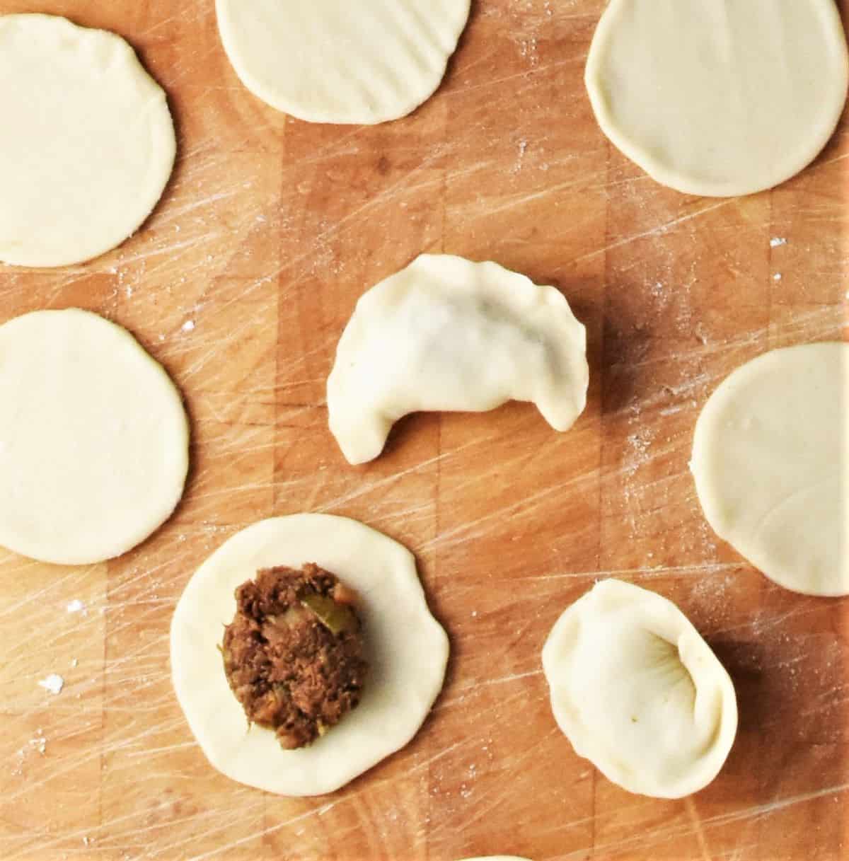 Adding filling to uszka dumplings on top of wooden surface.