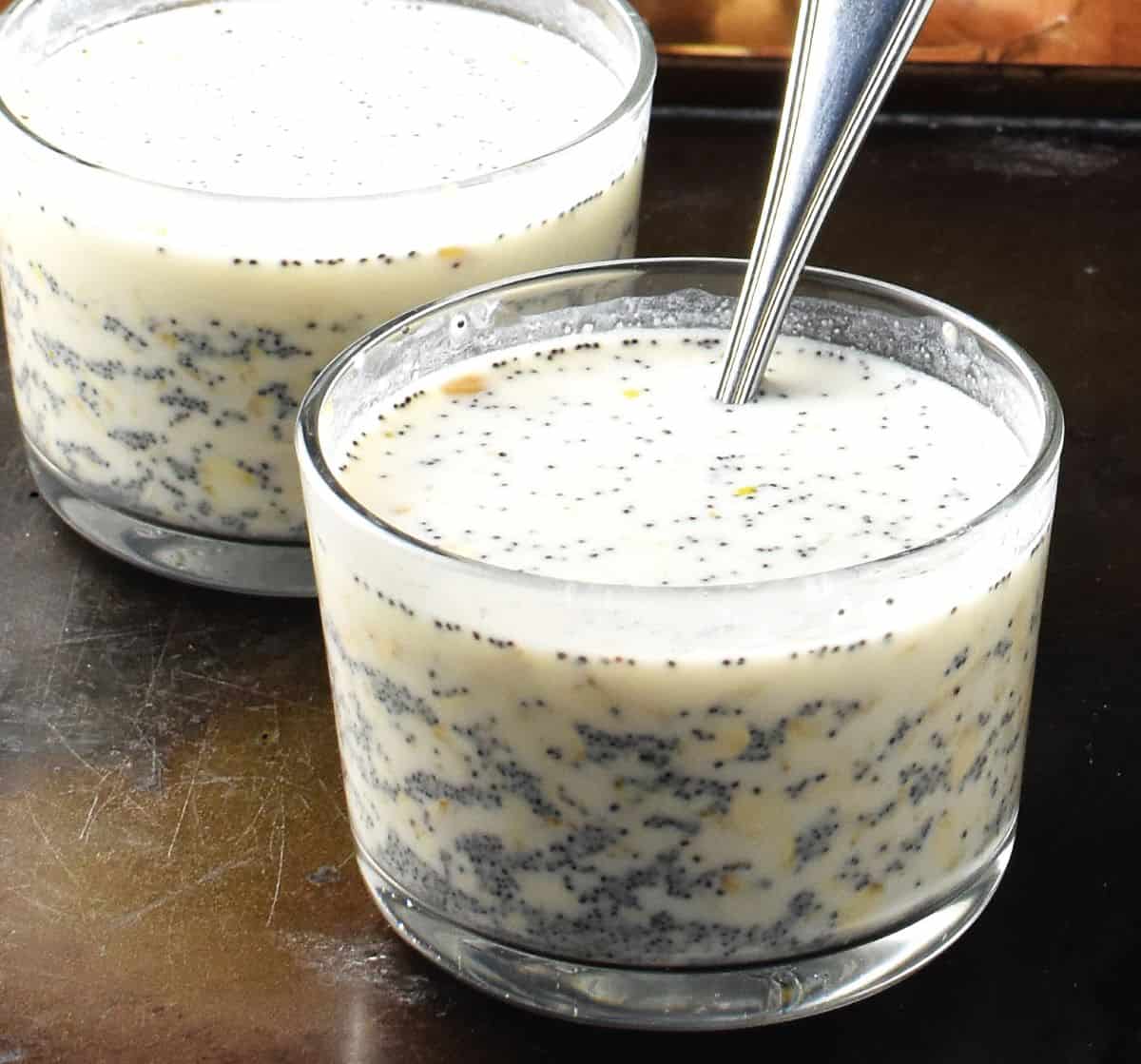 Side view of oats and poppy seeds with milk in 2 glasses with spoon.