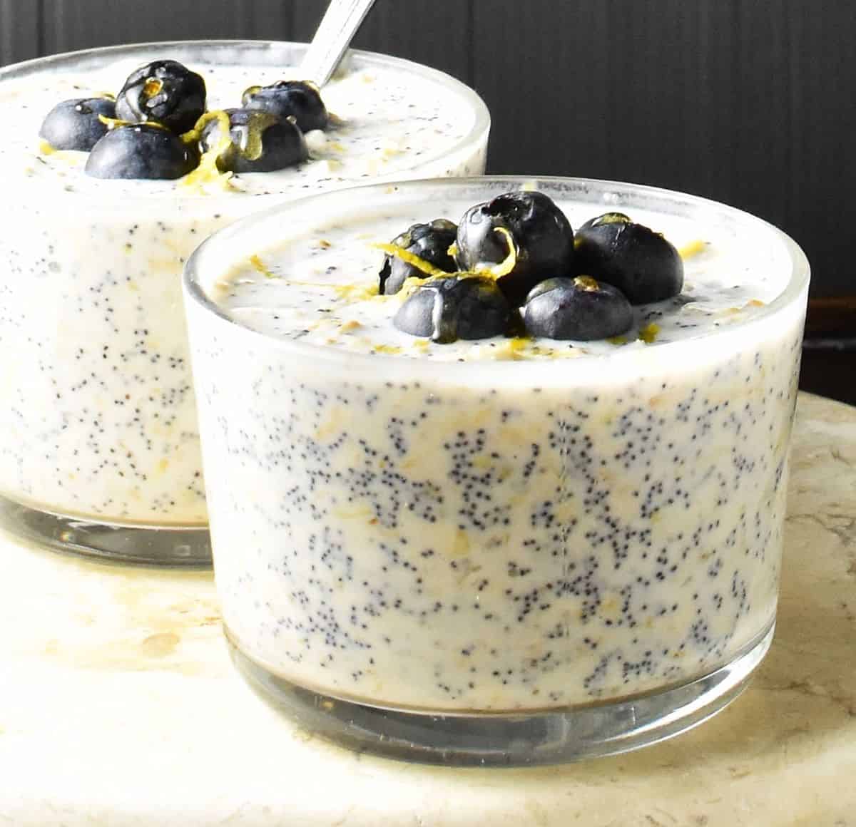 Close-up view of overnight oats with poppy seeds in 2 glasses topped with blueberries.