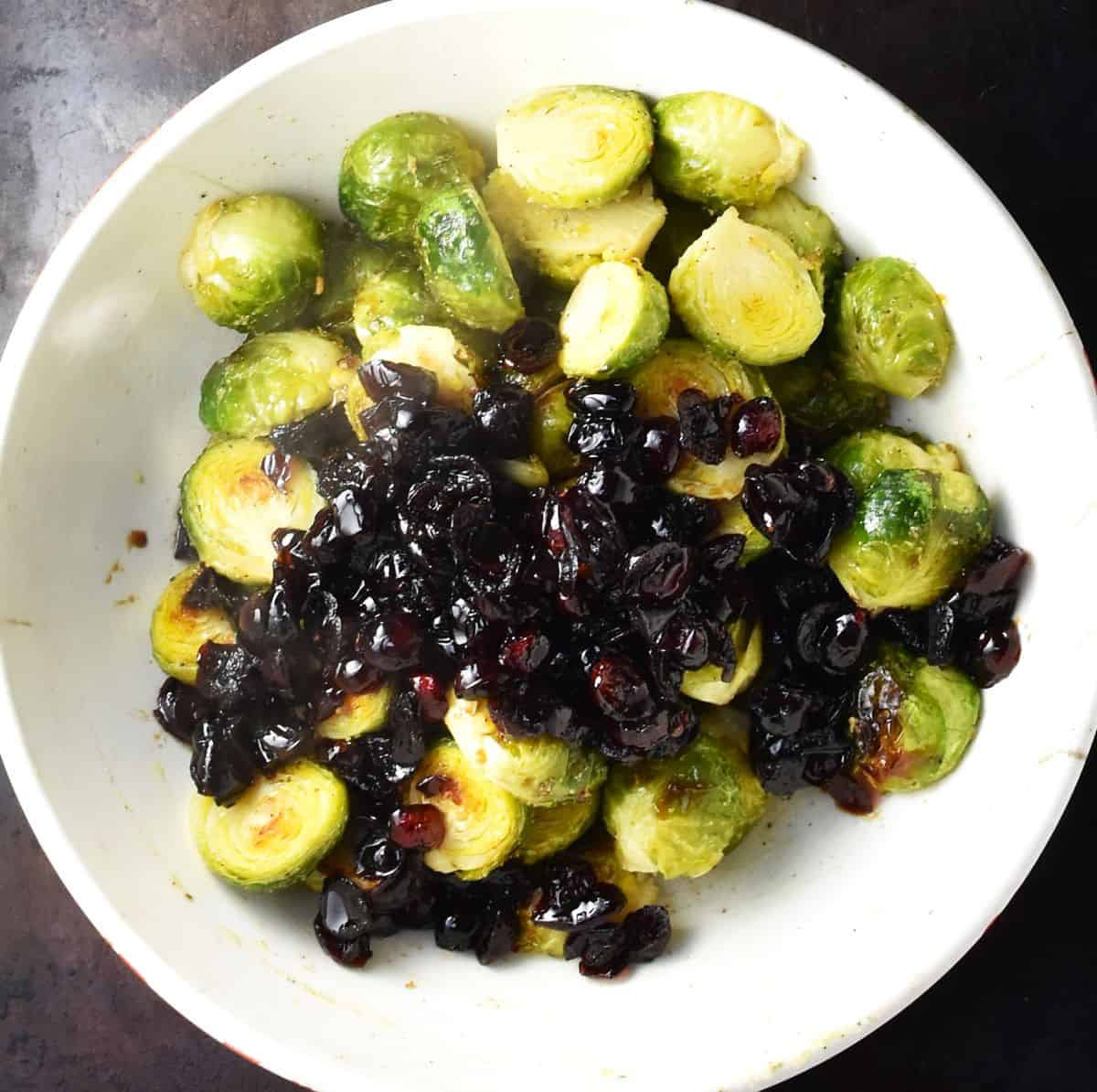 Top down view of halved brussels sprouts with cranberry glaze in white bowl.
