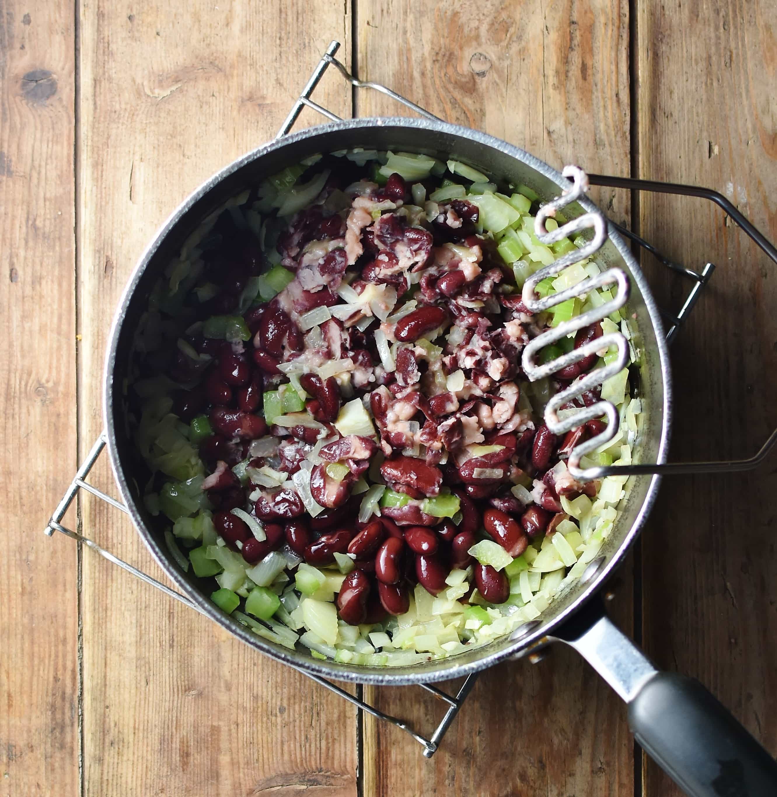 Kidney beans and chopped onions in large pot with potato masher.