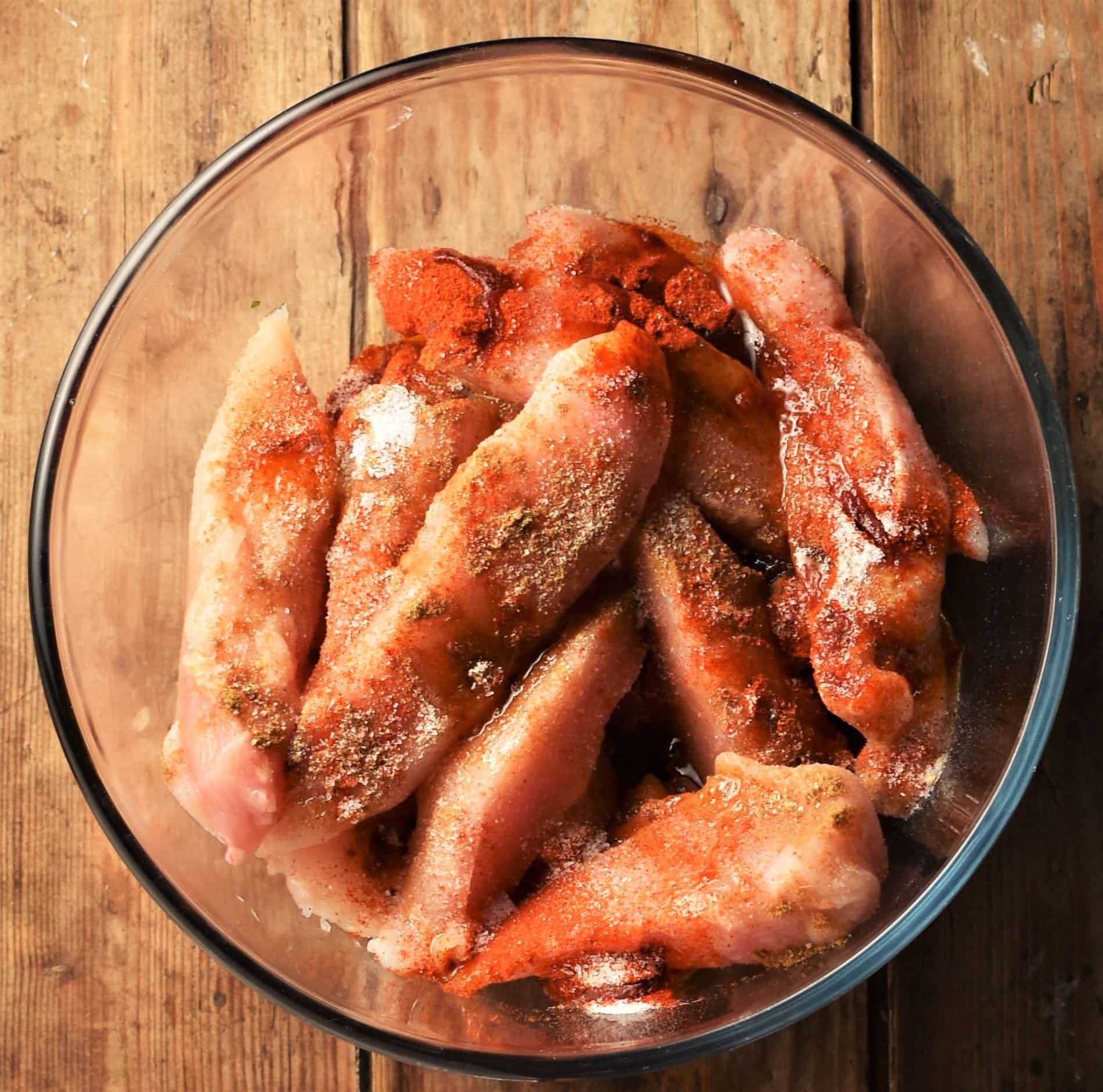 Chicken strips with spices in mixing bowl.