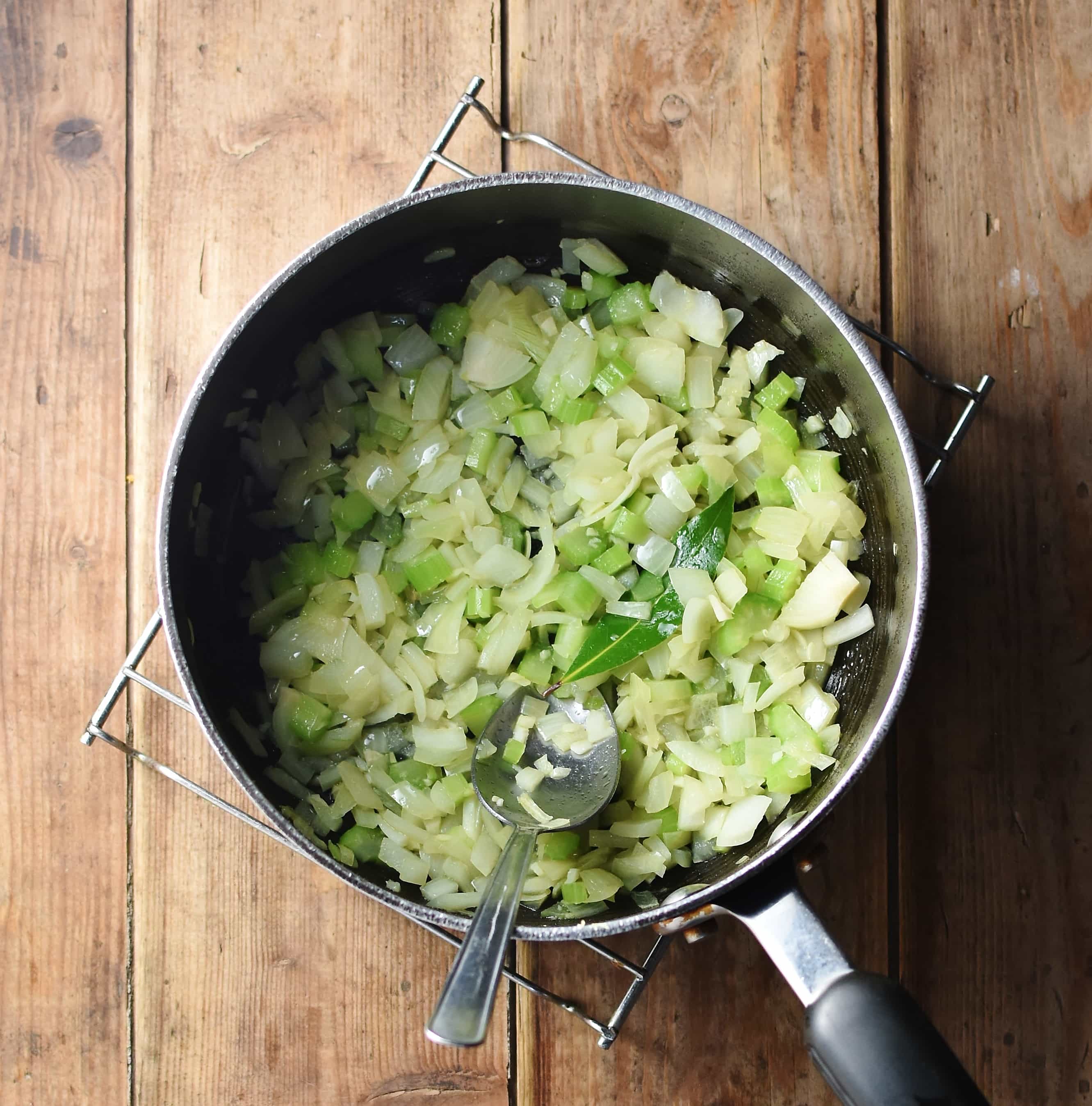 Chopped onions and celery in large pot with spoon.