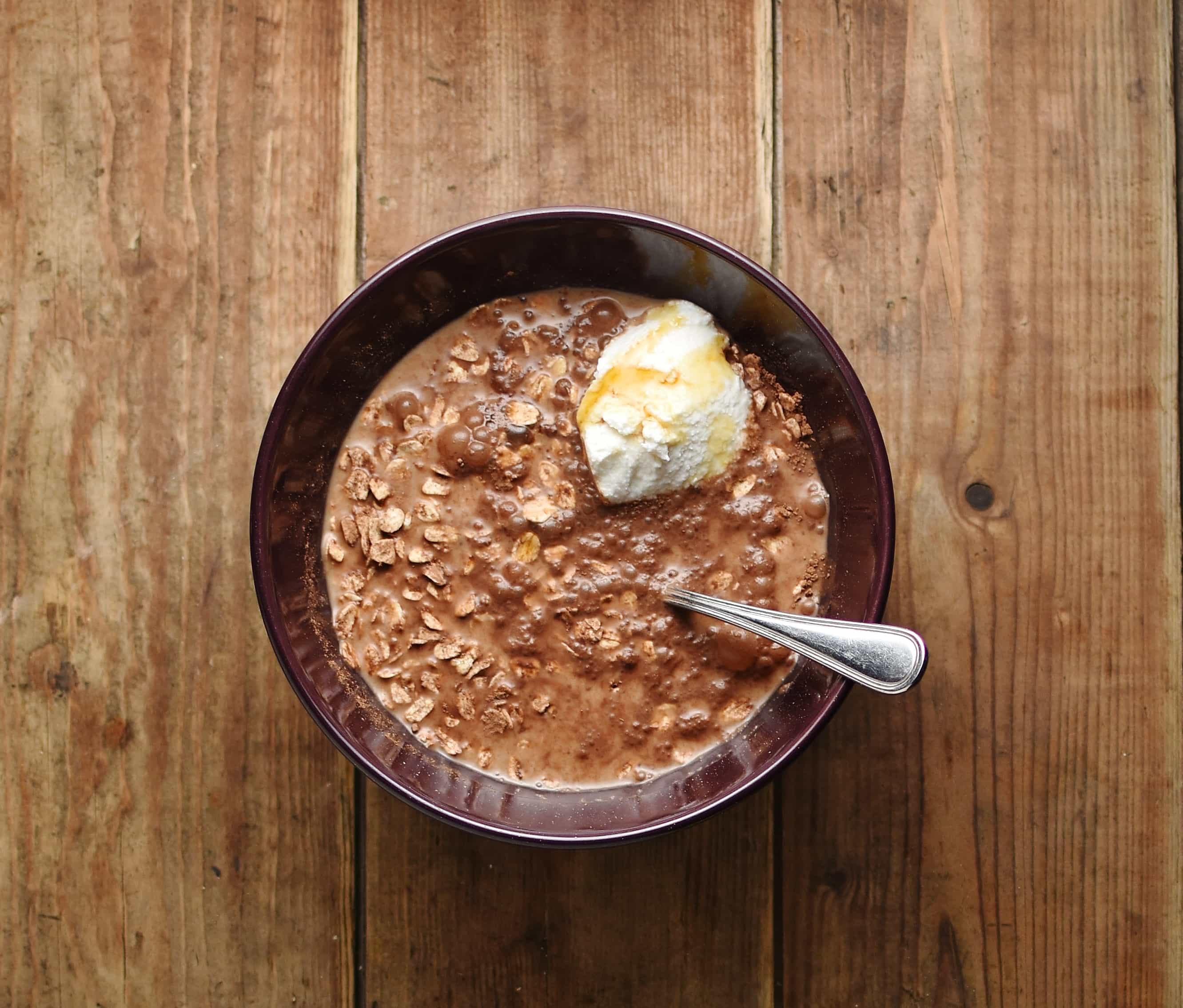Overnight oats with chocolate, cheese and spoon inside purple bowl.
