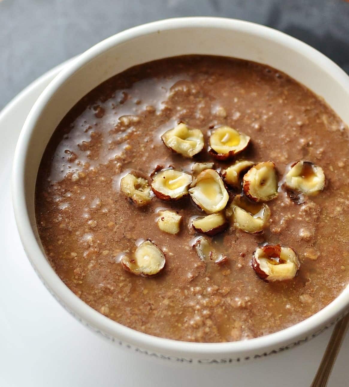 Top down view of chocolate oats topped with crushed hazelnuts in white cup on top of white saucer.