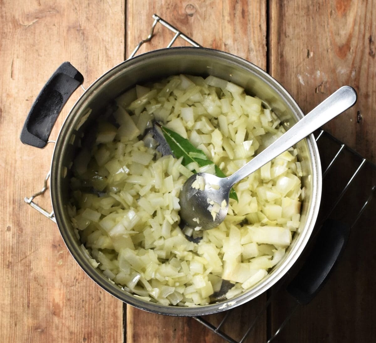 Onion mixture with bay leaf in pot with spoon.