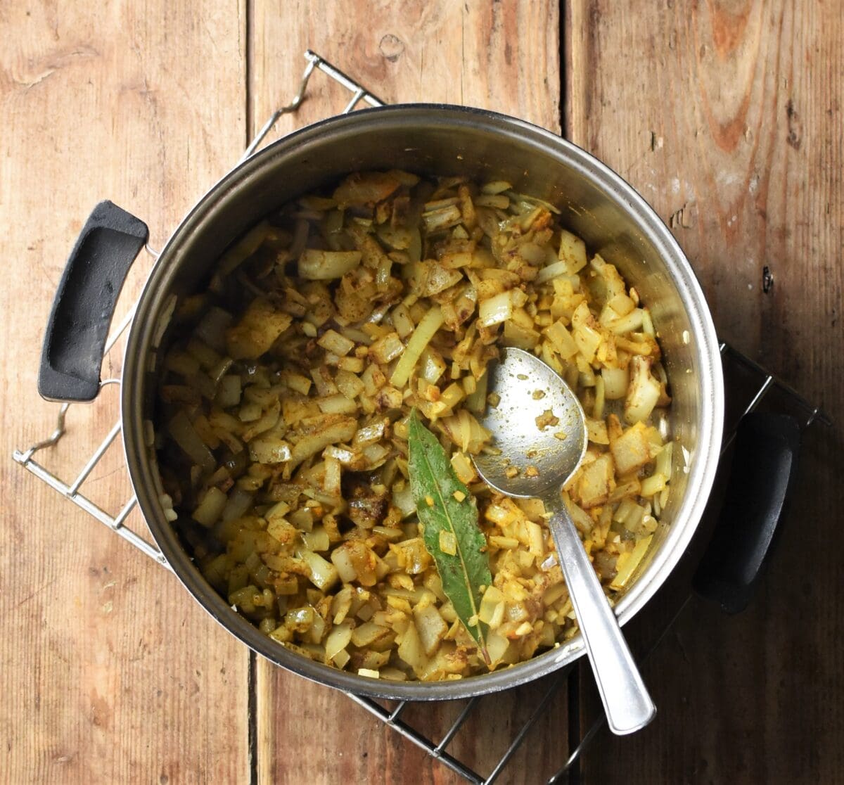 Onion mixture with spices and bay leaf in pot with spoon.