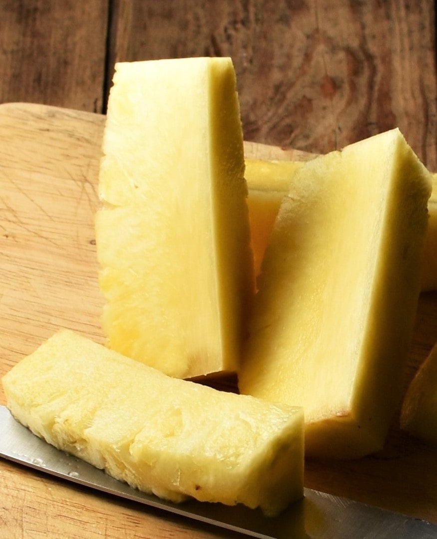 Long peeled pineapple slices on top of cutting board with knife.