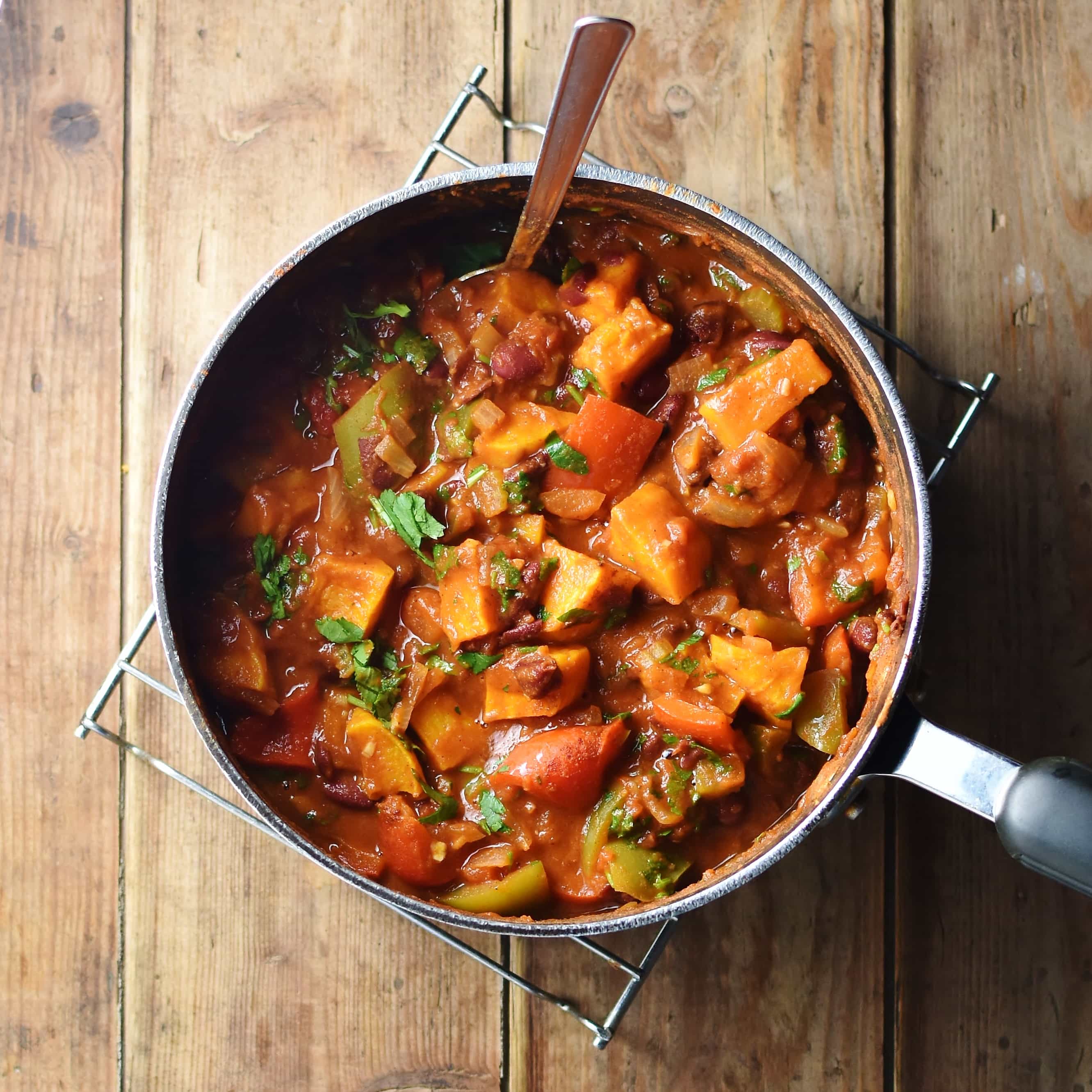 Squash, tomato chili with herbs in large pot with spoon.