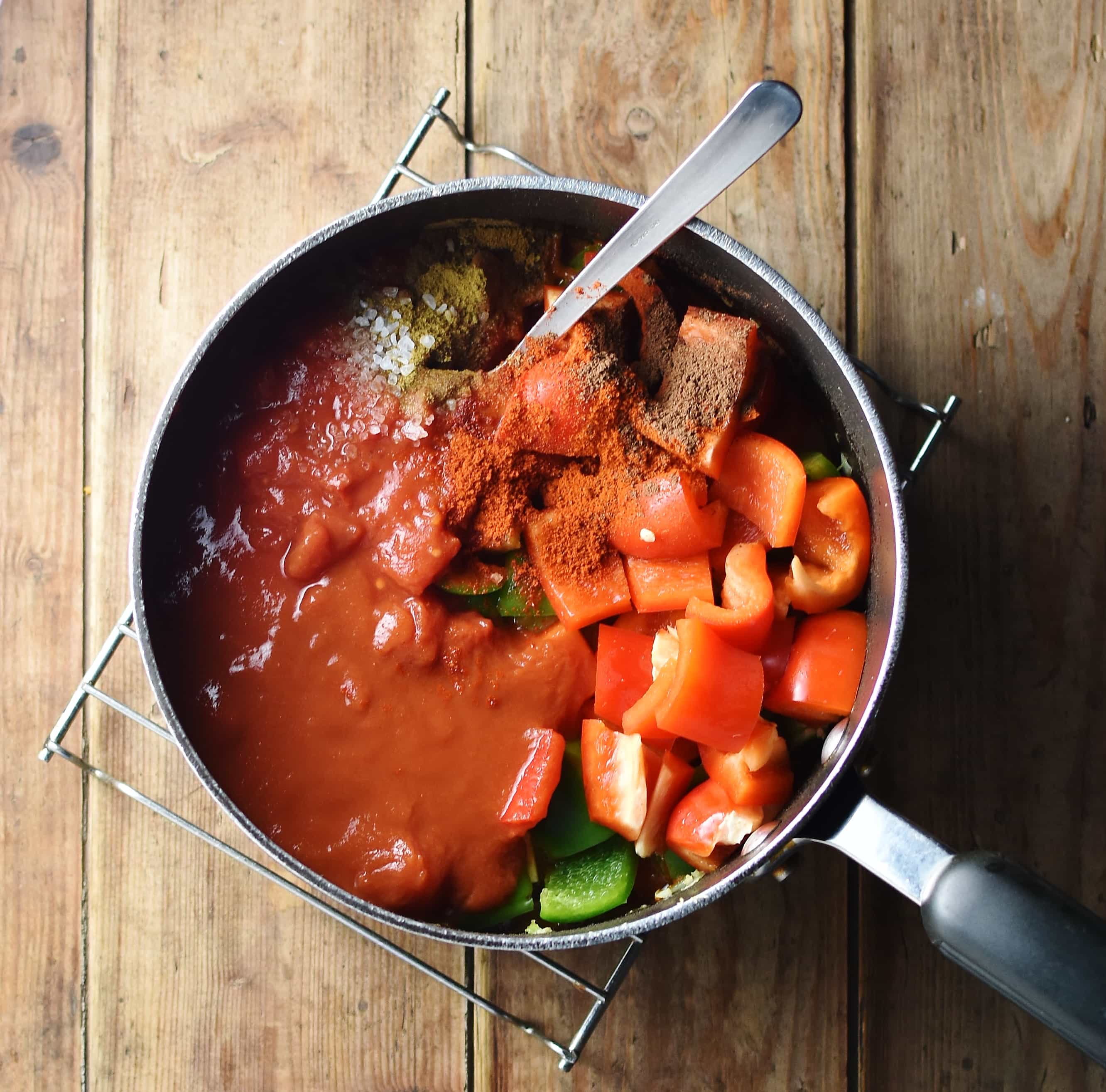 Chopped red pepper, tomatoes and spices in large pot with spoon.