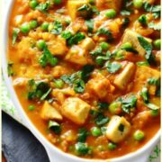 Top down view of tofu curry with peas in white oval dish.