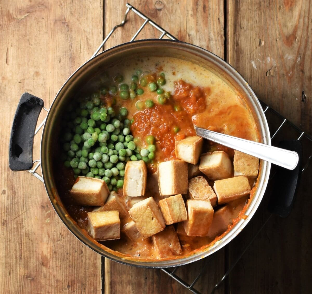Cubed tofu, peas and tomato sauce in pot with spoon.