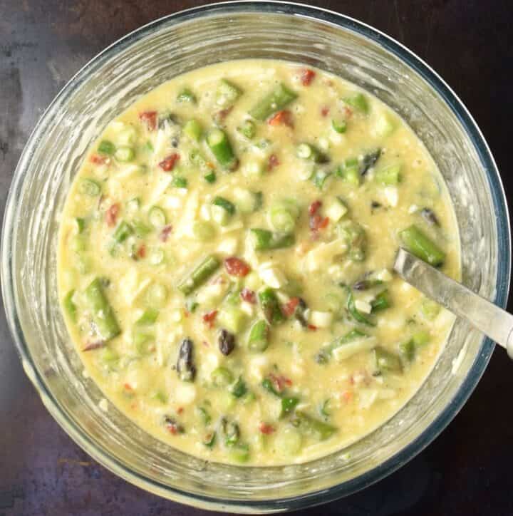 Top down view of egg asparagus muffin batter in glass bowl with ladle.