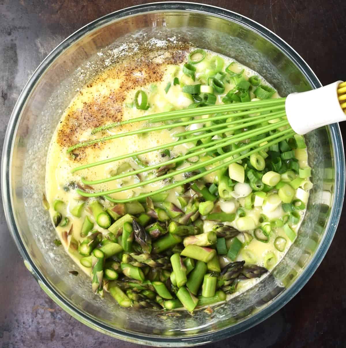 Chopped asparagus and scallions with egg mixture in bowl with whisk.