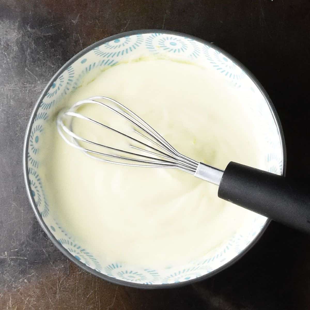 Top down view of creamy dressing in small bowl with whisk.
