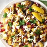 Top down close-up view of curried cauliflower salad with creamy dressing and lemon wedges on large plate.