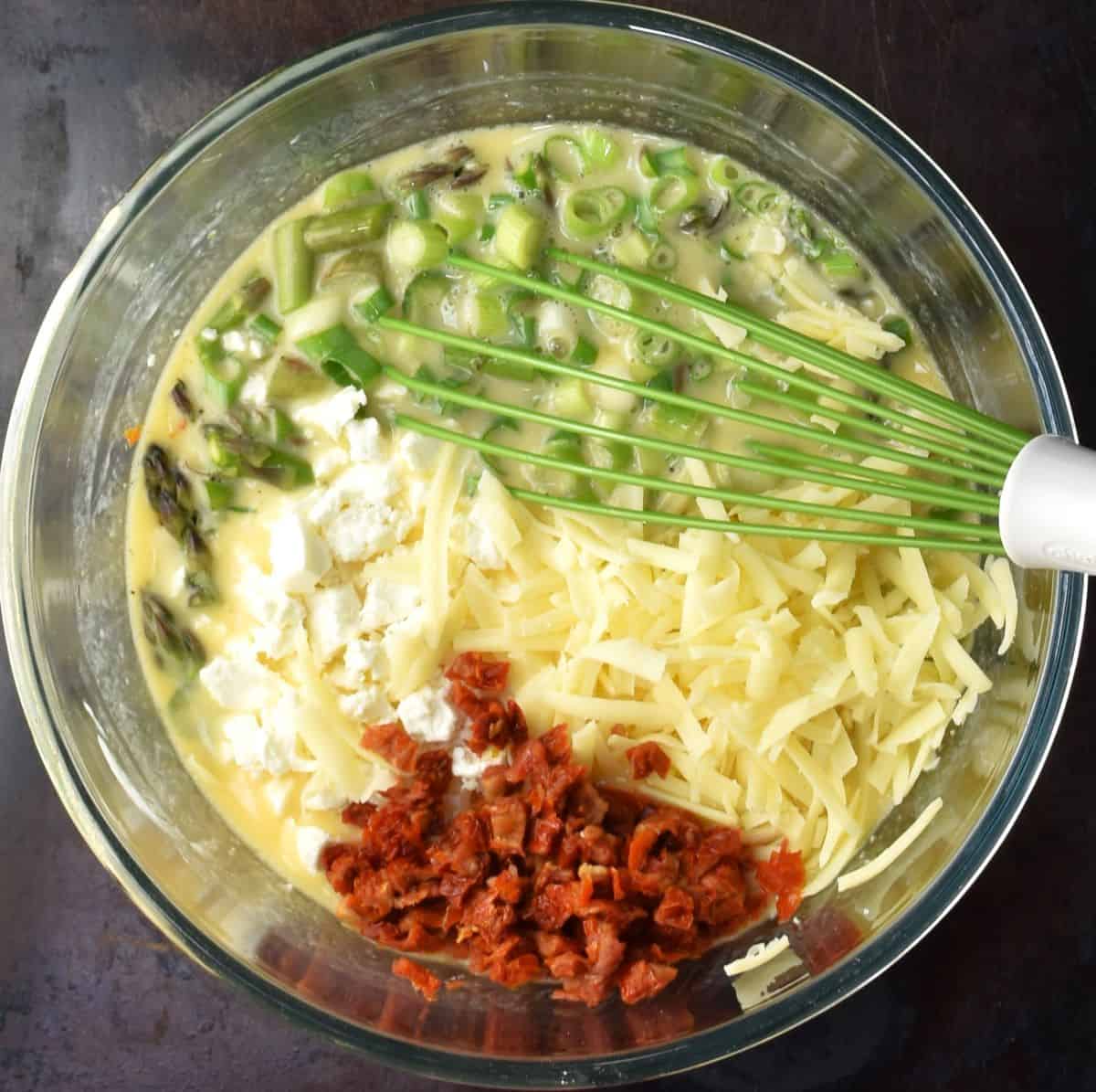 Asparagus egg muffin mixture with cheese and tomatoes and whisk.