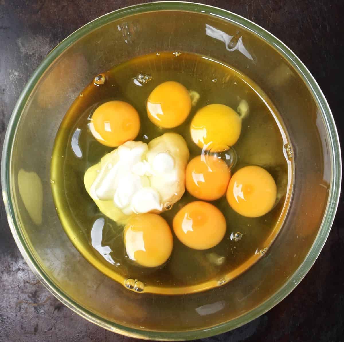 Top down view of 7 raw eggs with yogurt in glass bowl.