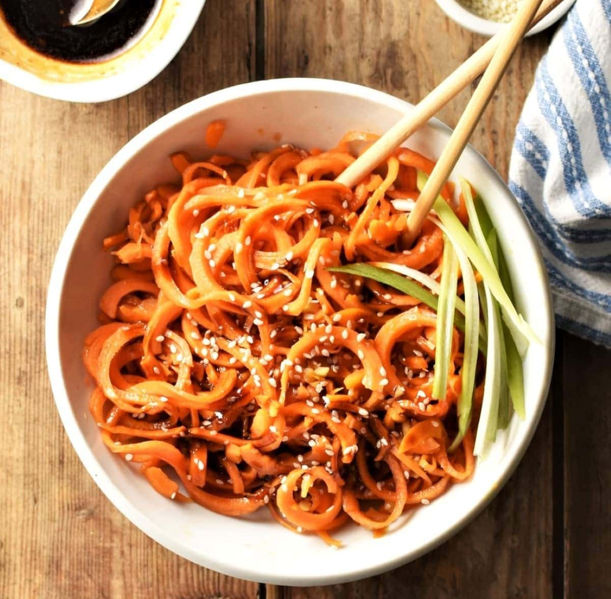 Stir fried carrot noodles in white bowl with chopsticks.