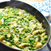 Leek stew with peas and potato dumplings in black cast iron oval casserole dish with steam visible and blue-and-white cloth in background.