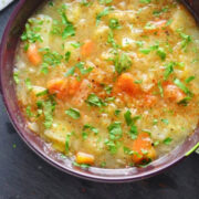 Sauerkraut soup in purple bowl with knife and bread in background.