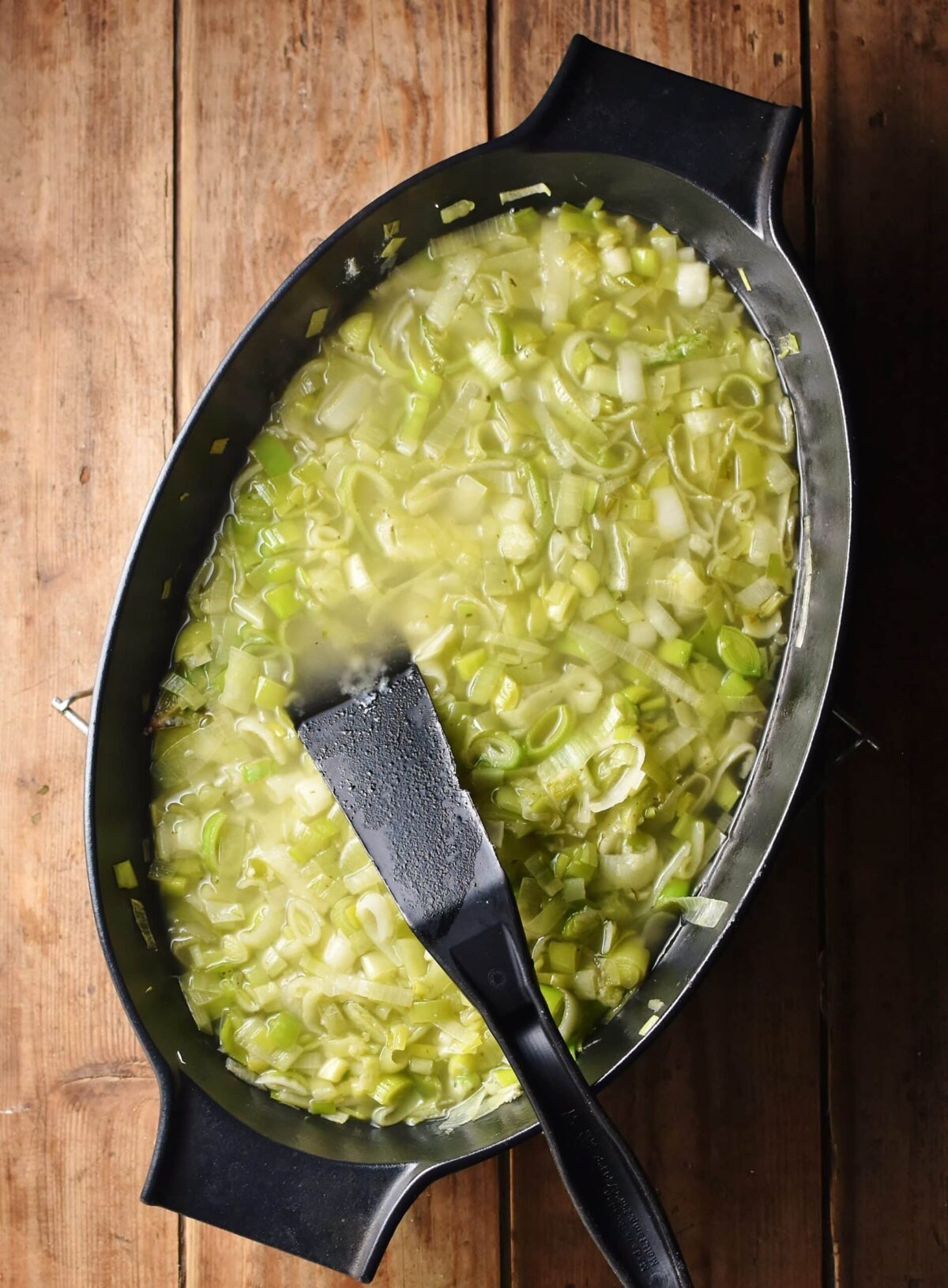 Leek stew with black spatula in black, oval shallow dish.