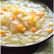 Partial close-up view of sauerkraut soup in purple bowl with herbs in background.