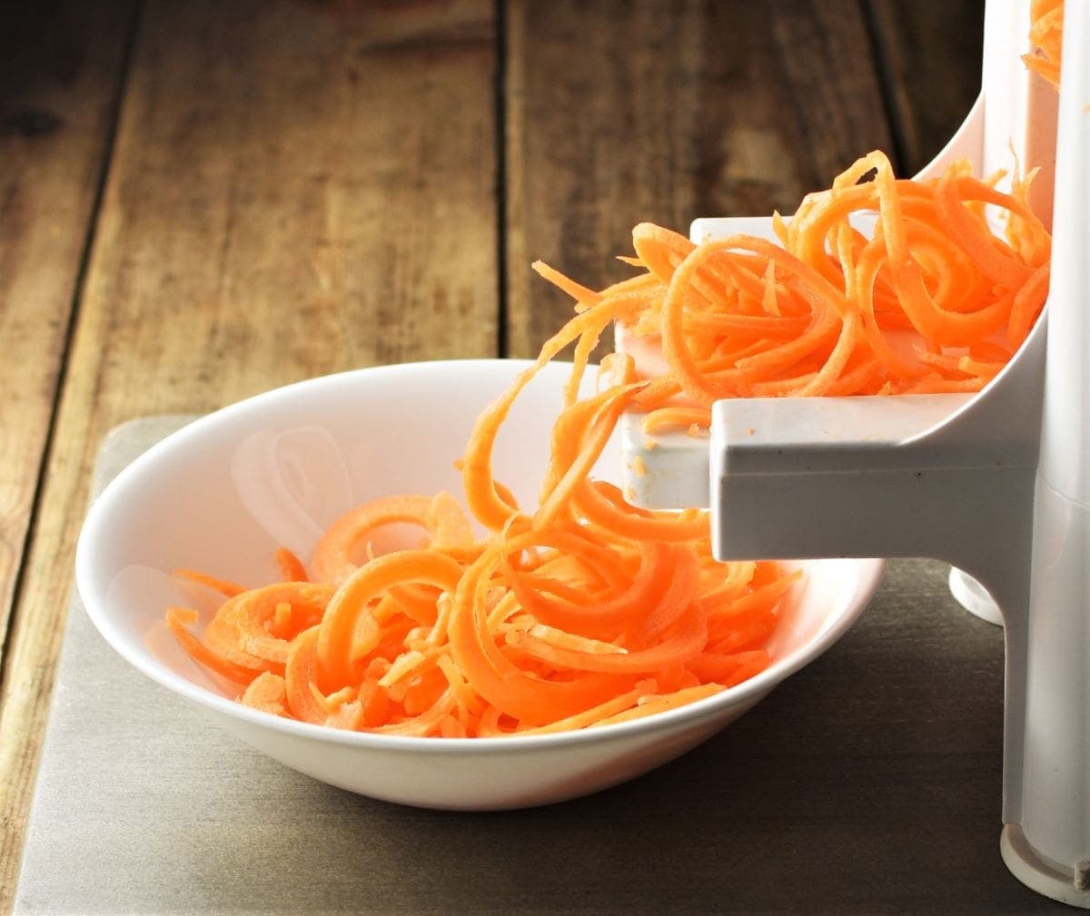 Spiralized carrot in white bowl and spiralizer.