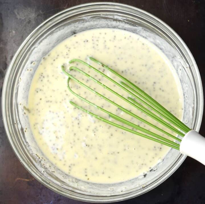 Top down view of chia seed pancake batter in glass bowl with whisk.
