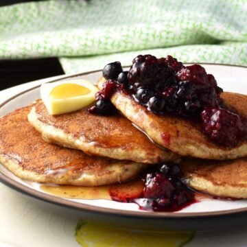 Side view of chia pancakes with fruit and maple syrup on top of plate.