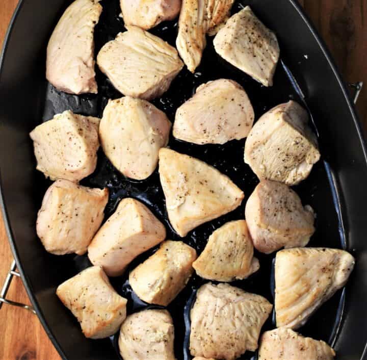 Chicken pieces in black, oval casserole dish.
