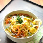 Spiralized vegetable soup in white bowl with green cloth on oven tray.
