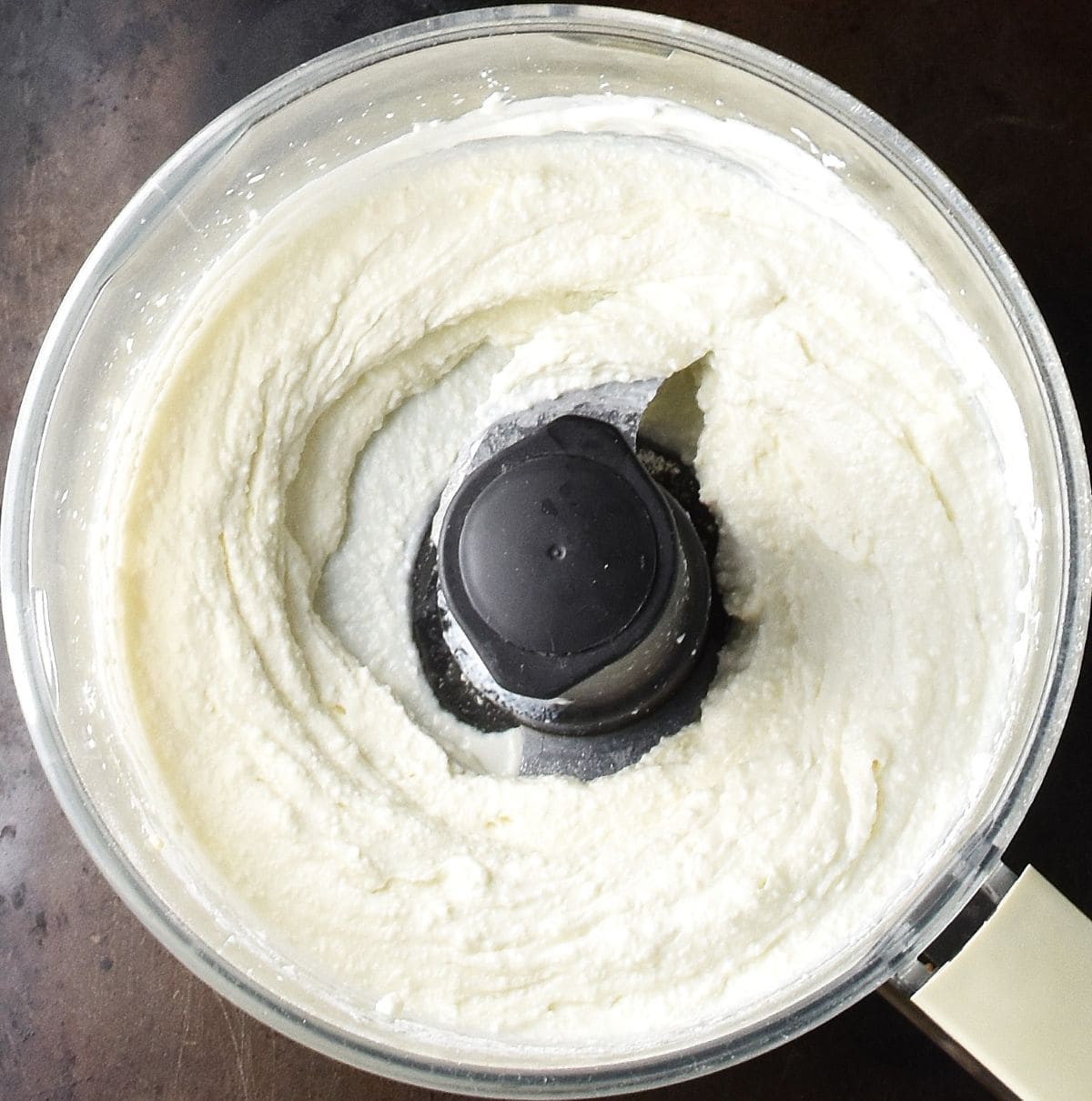 Top down view of creamy twarog cheese in food processor bowl.