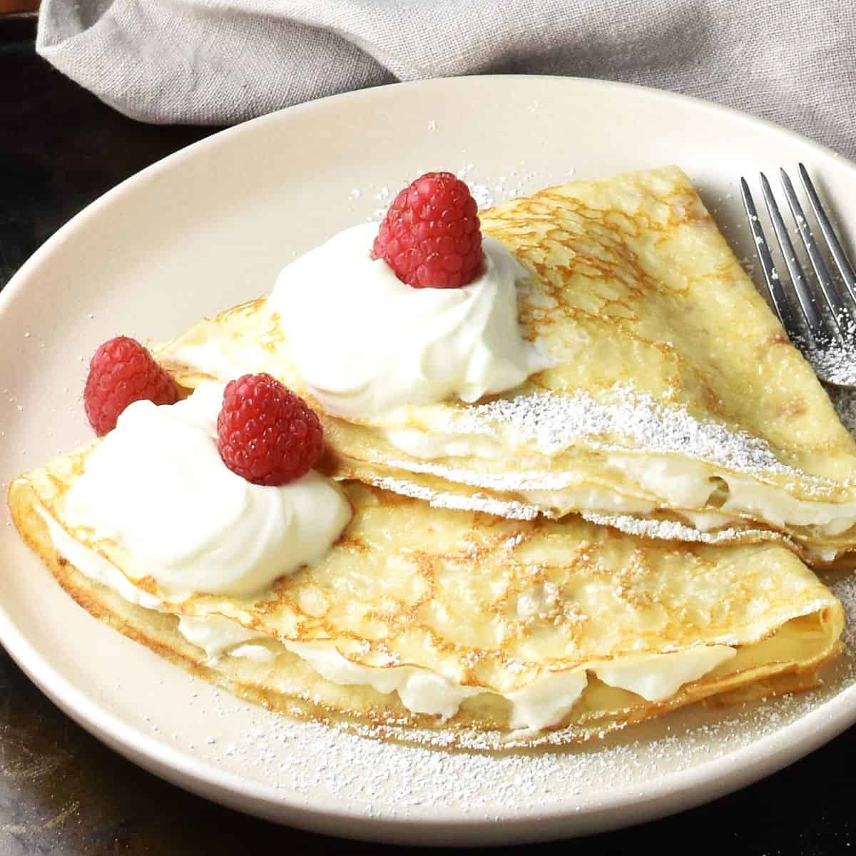 Side view of 2 folded Polish crepes with sour cream and fruit on pink plate.