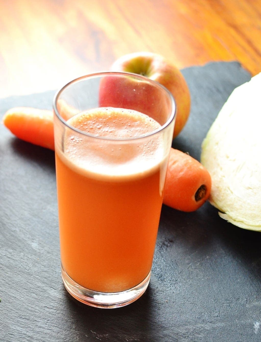Cabbage juice in glass with carrot and apple on slate surface.