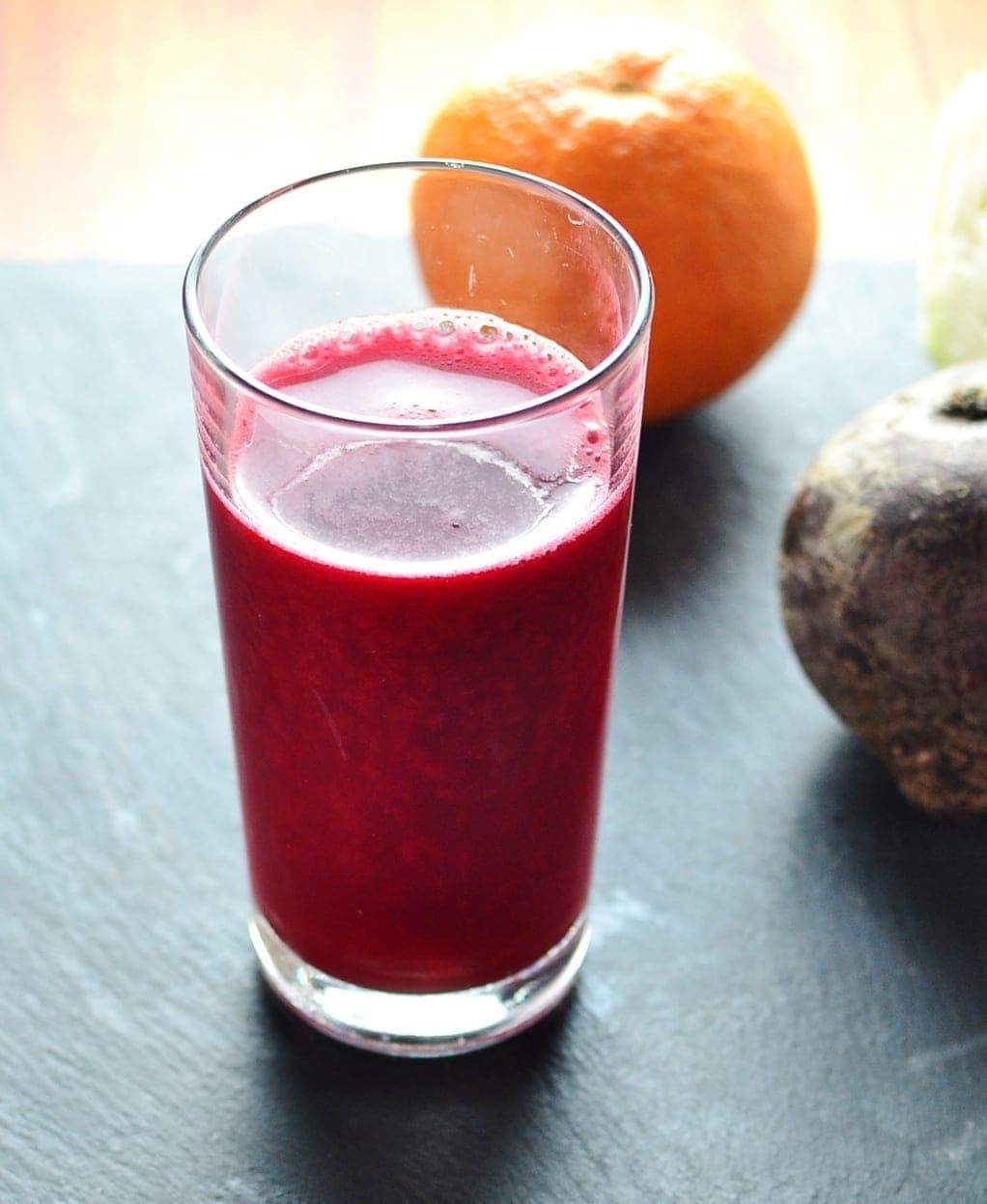 Cabbage juice with orange and beetroot in glass on slate surface.